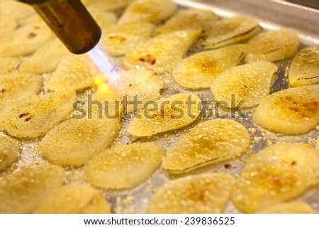 Blowtorch caramelizing sugar on pear slices. - stock photo