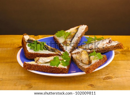 Tasty sandwiches with sprats on plate on wooden table on brown ...