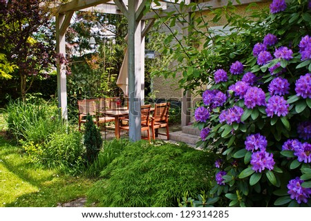 Outdoor patio with wooden table and chairs and flowering rhododendron 