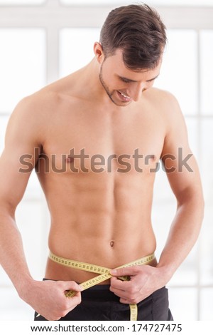 Keeping body in perfect shape. Young muscular man measuring his waist 