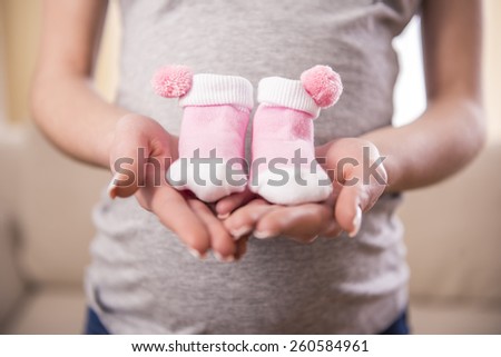 Pregnant woman is holding belly on the little socks for babies. - stock photo