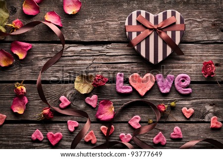 Word Love with Heart shaped Valentines Day gift box on old vintage wooden plates. Sweet holiday background with rose petals, small hearts, curved ribbon. - stock photo