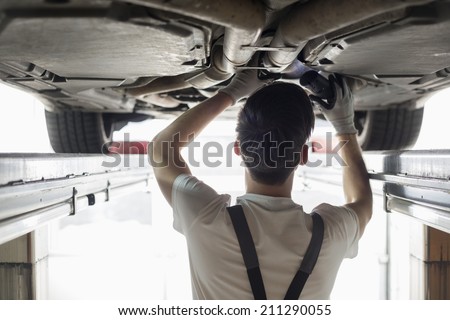 Rear View Of Automobile Mechanic Examining Car In Workshop Stock