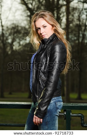 Pretty young woman long blond hair in winter forest wearing black leather jacket and blue shirt