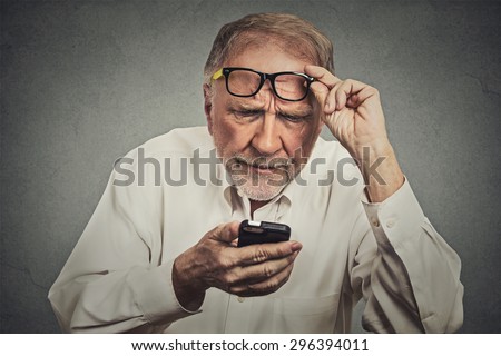 Closeup portrait headshot elderly man with glasses having trouble seeing cell phone has vision problems. Bad text message. Negative human emotion facial expression perception. Confusing technology - stock photo