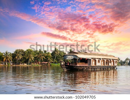 House boat in backwaters near palms at dramatic sunset sky in alappuzha, Kerala, India - stock photo