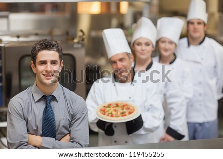 Waiter standing in front of Chef's holding a pizza - stock photo