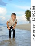Small photo of Full growth portrait on a tropical beach: handsome 8 years old boy in wet clothes without shoos ankle-deep in water. Leaned his hands on legs