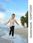 Small photo of Full growth portrait on a tropical beach: handsome 8 years old boy in wet clothes without shoos ankle-deep in water. Running fast