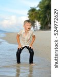 Small photo of Full growth portrait on a tropical beach: handsome slim 8 years old boy in wet clothes without shoos ankle-deep in water. Leaned his hands on legs, ready for a jump