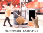 Small photo of Man use mobile phone, blurred image of the cleaning staff in the mall as background.(Building cleaning service is just a phone call away.)