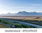 Small photo of The morning sun shines on the rippling waters of the Turnagain Arm as the Alaskan Railroad Tracks pass along its waters and to the Kenai Peninsula of Alaska.