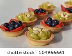 Small photo of Individual small cakes with fresh fruits (red and green grapes,banana,strawberry). Mini fruit tarts. Catering food. Sensational desserts that can be thrown together at the last minute.