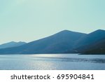 Small photo of Pyramidal mountain chain across the seashore of Aegean Sea in Greece. Landscape that combines mountains, sea, blue sky and sun light. Road across the mountain chain.
