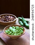 Small photo of Raw broad beans (lat. Vicia faba) in bowl with pods and roasted broad beans in the back, photographed with natural light (Selective Focus, Focus one third into the beans)