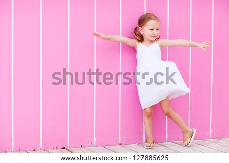 Full body portrait of adorable little girl outdoors against pink wall
