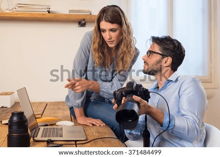 Young photographers looking at photographs on laptop. Assistant photographer helping photographer in the selection of photos. Young team of photographer working in a professional studio.