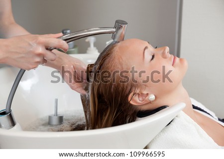 Side view of a beautiful young woman getting a hair washed by hairdresser at salon