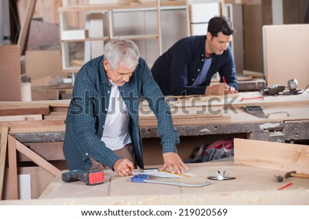 Senior male carpenter drawing diagram on blueprint with colleague in 