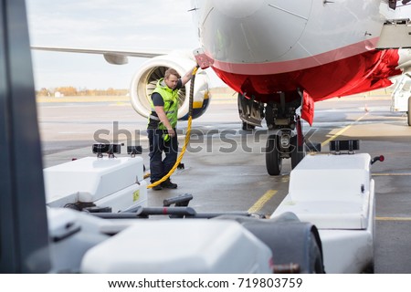 Mid Adult Crew Member Charging Airplane On Runway