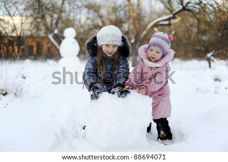 Two sisters rolling snow to make snowman
