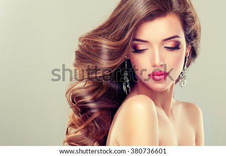 Beautiful model brunette with long curled hair and jewelry earrings