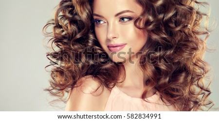 Brunette girl with long and volume shiny wavy hair . Beautiful model with curly hairstyle .