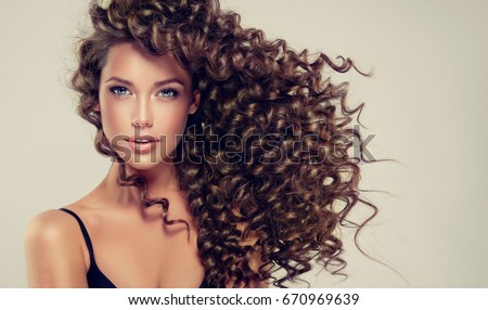 Brunette girl with long and shiny curly hair . Beautiful model woman with wavy hairstyle