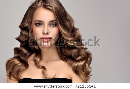 Brunette girl with long and shiny curly hair . Beautiful model woman with curly hairstyle .Care and beauty of hair