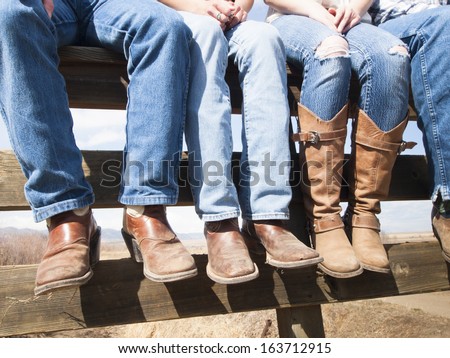 Cowboys and cowgirls sitting on wooden fence. - stock photo