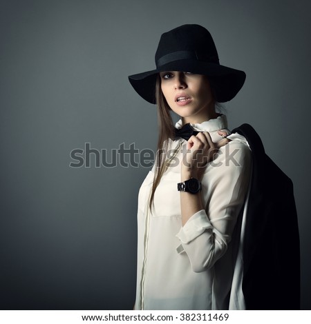 Young beautiful sexy woman in jacket, white shirt, bow-tie and hat over gray background. Fashion female portrait. Tomboy. Girl gets on men's clothes.
