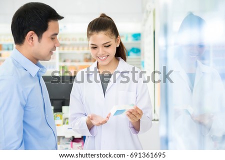Female pharmacist holding medicine bottle giving advice to customer in chemist shop or pharmacy