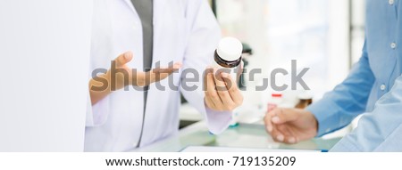 Female pharmacist holding medicine bottle giving advice to customer in chemist shop or pharmacy - horizontal web banner with copy space on the left