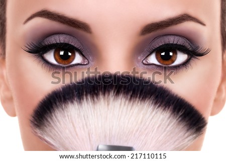 Beautiful woman with brown eyes wearing eye shadow and holding makeup brush