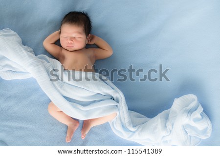 Newborn 4 day old baby boy lying on his back relaxing under a blue wrap cloth