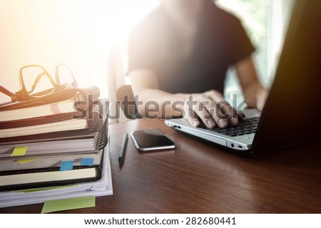 designer hand working with  digital tablet and laptop and notebook stack and eye glass on wooden desk in office