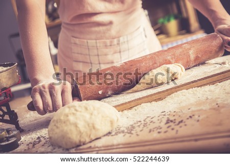 Close up of female baker hands kneading dough and making bread with a rolling pin. Retro look.