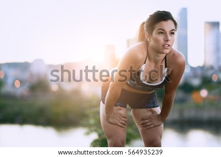 Portrait of active millenial woman jogging at dusk with an urban cityscape and sunset in the background