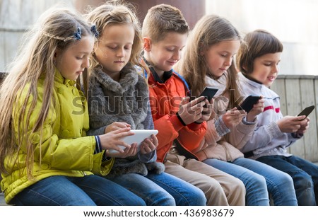 Ordinary kids sitting with mobile devices in street