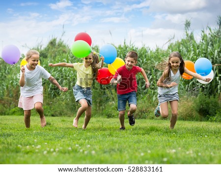 cheerful smiling boy and girls holding air balloons and running in summer park. Selective focus