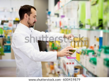 Smiling male pharmacist searching for reliable drug in pharmacy