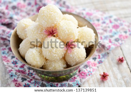 Homemade coconut balls decorated with little pink flowers in metal bowl, wooden background - stock photo