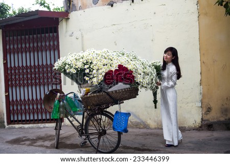 HANOI, VIETNAM - NOVEMBER 23: Vietnamese girl in traditional dress buying white daisy flower on street in Hanoi on November 23, 2014 in Hanoi, Vietnam. White daisy flowers bloom in November.