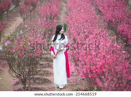 Beautiful Vietnamese girl with traditional dress (ao dai) is in peach flower garden in Hanoi, Vietnam