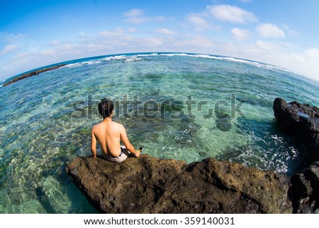 LYSON, VIETNAM - JANUARY 4, 2016: Young man sit on rock near the beautiful beach in Ly Son island in Quang Ngai, Vietnam.