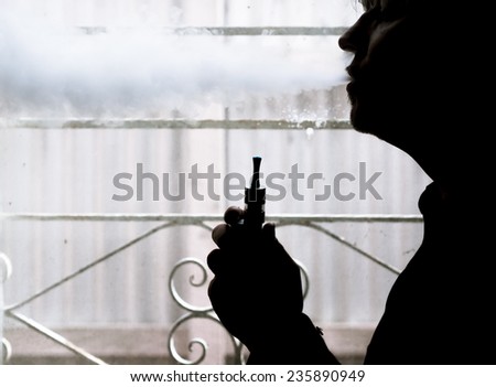 Silhouette of a man using an electronic cigarette (vaping) at home ...