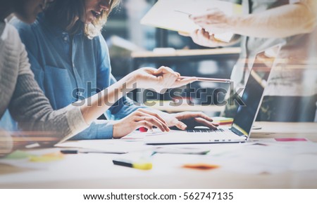 Teamwork,brainstorming concept.Young creative managers team working with new startup project in modern office. Contemporary notebook on wood table.Horizontal, film effect