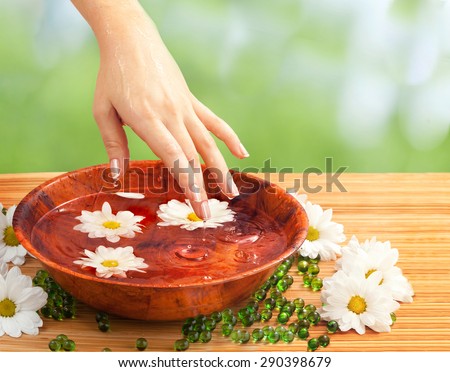 Spa Salon: Beautiful Female Hand with French Manicure in the Bamboo Bowl of Water with White and Yellow Flowers on the Straw Mat at the Nature Background