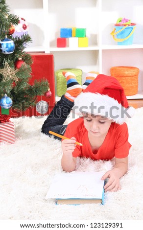 Little boy in Santa hat writes letter to Santa Claus