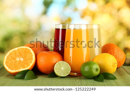 Glasses of juise with leafs and fruits on table on bright background